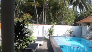 A swimming pool with a white deck, surrounded by palm trees and a white wall. - Villa Comfort (Hikkaduwa)