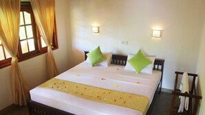 A hotel room with a bed, two bedside tables, a nightstand, a window with curtains, and wall-mounted lights. - Villa Comfort (Hikkaduwa)