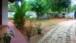 A covered outdoor area with a wooden bench, potted plants, and a paved walkway. - Villa Relax (Galle)