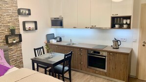 Una cocina moderna con armarios de madera, horno empotrado, lavamanos y cafetera. Hay una mesa de comedor con sillas y un florero con una flor.