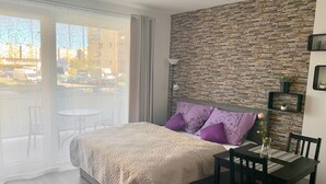A bedroom with a bed, a dining table, chairs, a stone wall, and a view of the outside. - RS Apartments (Olomouc)