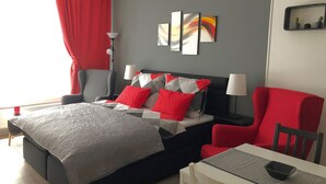 Una habitación de hotel moderna con una cama, un escritorio y una silla. Hay dos lámparas en el escritorio y una silla roja.