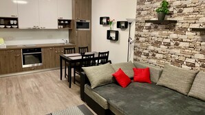 Una cocina moderna con armarios de madera, horno empotrado y comedor con sofá gris y cojines rojos.