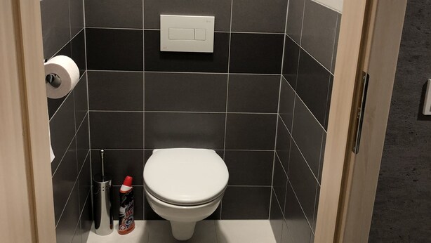 A compact bathroom with a toilet, a hand dryer, and a roll of toilet paper on the wall. - RS Apartments (Olomouc)