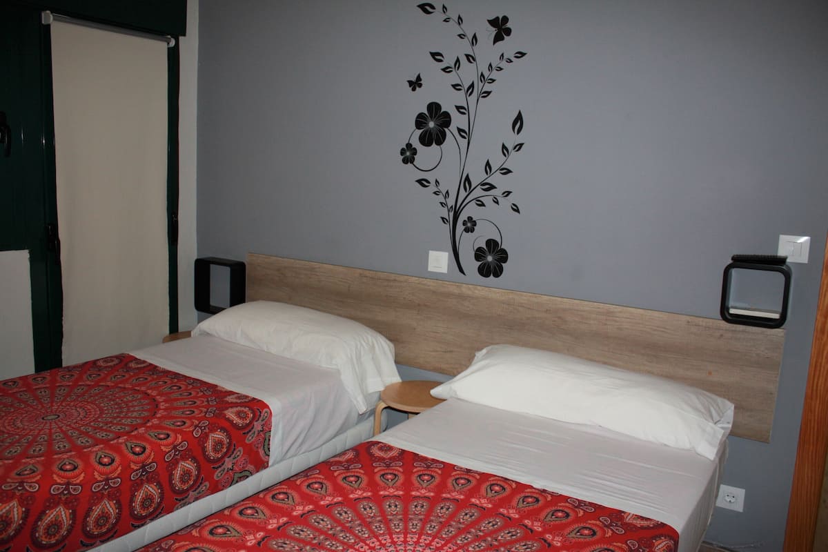 Une chambre d’hôtel avec deux lits, une tête de lit en bois, un mur décoré d’un motif floral et deux tables de chevet.