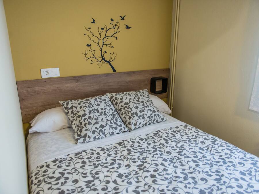 A bed with a patterned bedspread, a wooden headboard, and a wall decoration of a tree with birds.