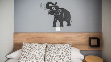 Een slaapkamer met een bed, twee kussens, een houten hoofdbord, een nachtkastje en een muursticker van een olifant.