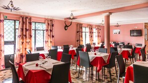 Un restaurant avec de nombreuses tables, chacune recouverte d’une nappe rouge, et des chaises disposées autour.