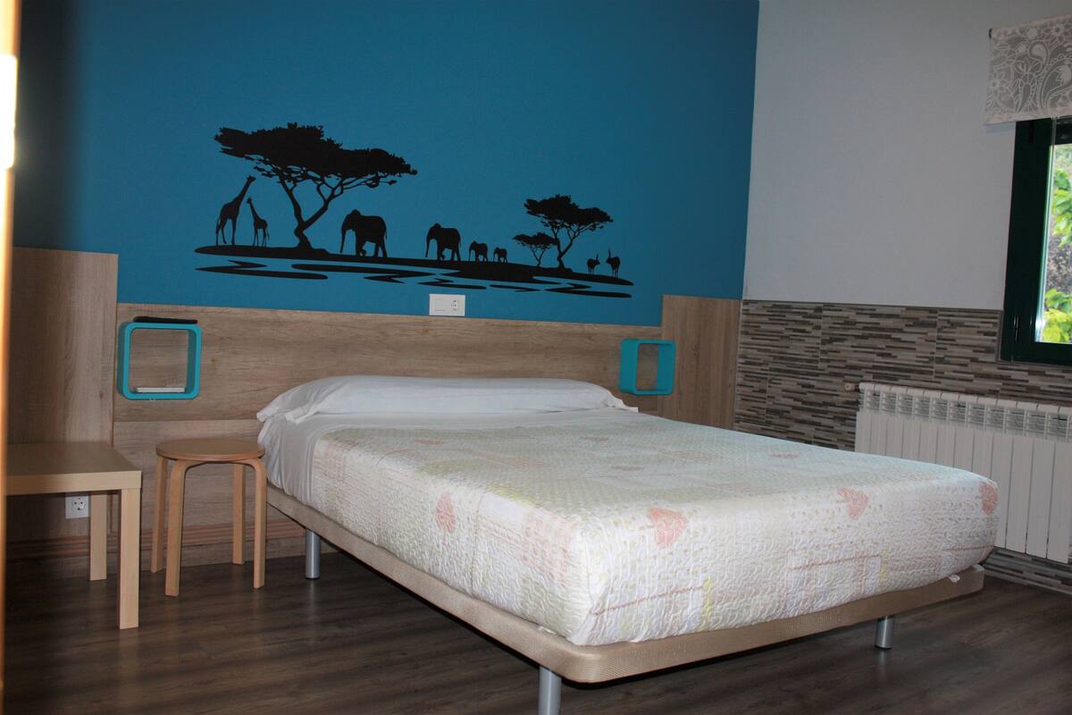Une chambre à coucher avec un lit, une table de chevet en bois, une petite table et un motif décoratif représentant des animaux sur le mur.