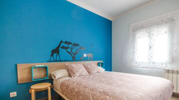 A bedroom with a bed, a nightstand, a small stool, a wall mural, and a window with a curtain.