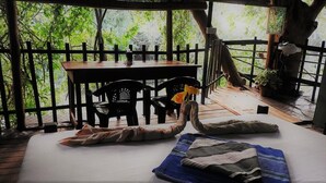 A room with a bed, a table, and chairs. There is a view of trees through a wooden fence. - Riverside Cabana Yala (Thissamaharama)