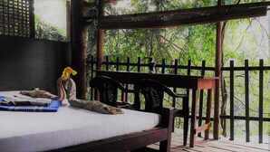 A bed with a white mattress and a blue mat, a wooden headboard, and a view of greenery through a wooden fence. - Riverside Cabana Yala (Thissamaharama)