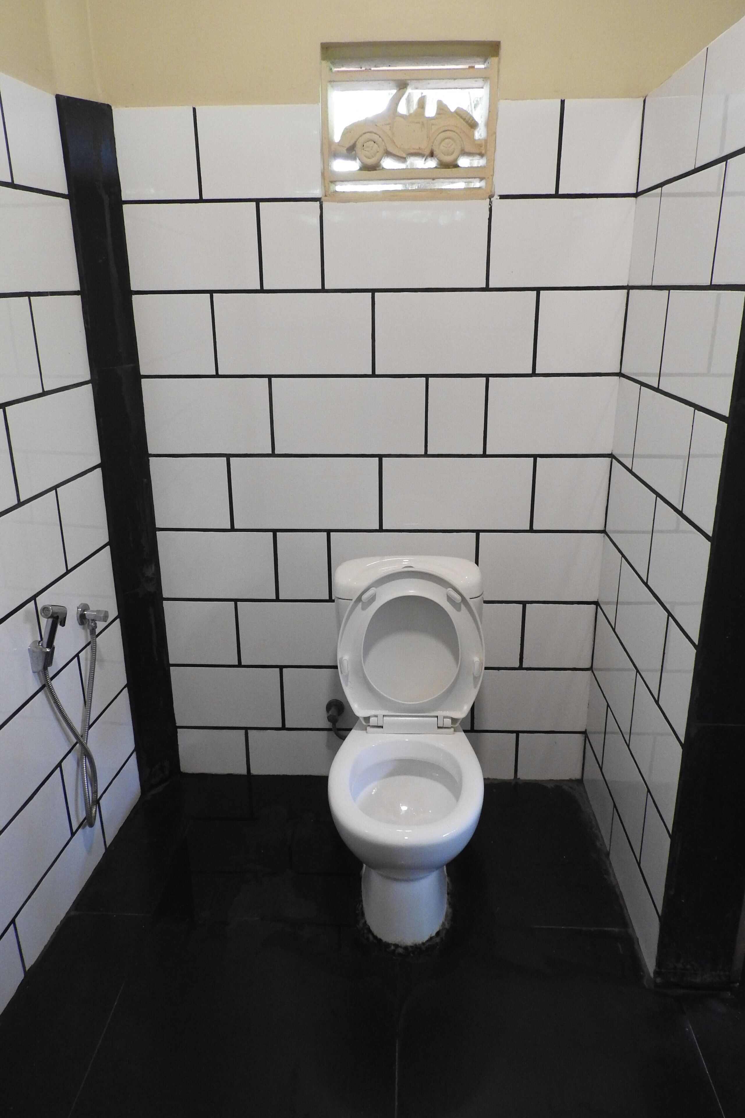 Een badkamer met een toilet, muren betegeld in zwart en wit, en een raam boven het toilet.