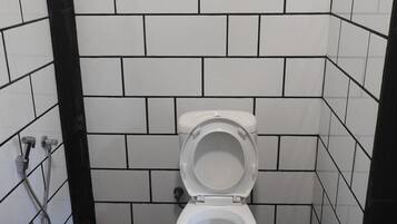Een badkamer met een toilet, muren betegeld in zwart en wit, en een raam boven het toilet.
