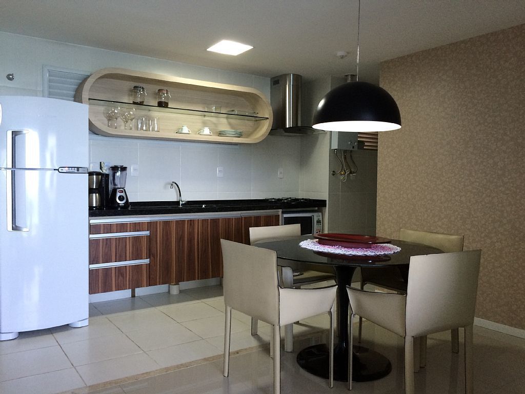 Una cocina moderna con un refrigerador blanco, una cafetera y un microondas. Hay una mesa de comedor con sillas y una lámpara colgante encima.