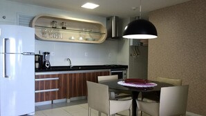 Una cocina moderna con un refrigerador blanco, una cafetera y un microondas. Hay una mesa de comedor con sillas y una lámpara colgante encima.