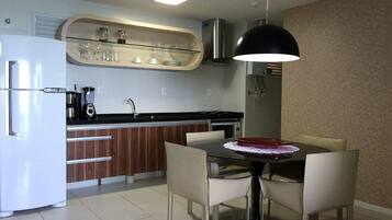 Una cocina moderna con un refrigerador blanco, una cafetera y un microondas. Hay una mesa de comedor con sillas y una lámpara colgante encima.
