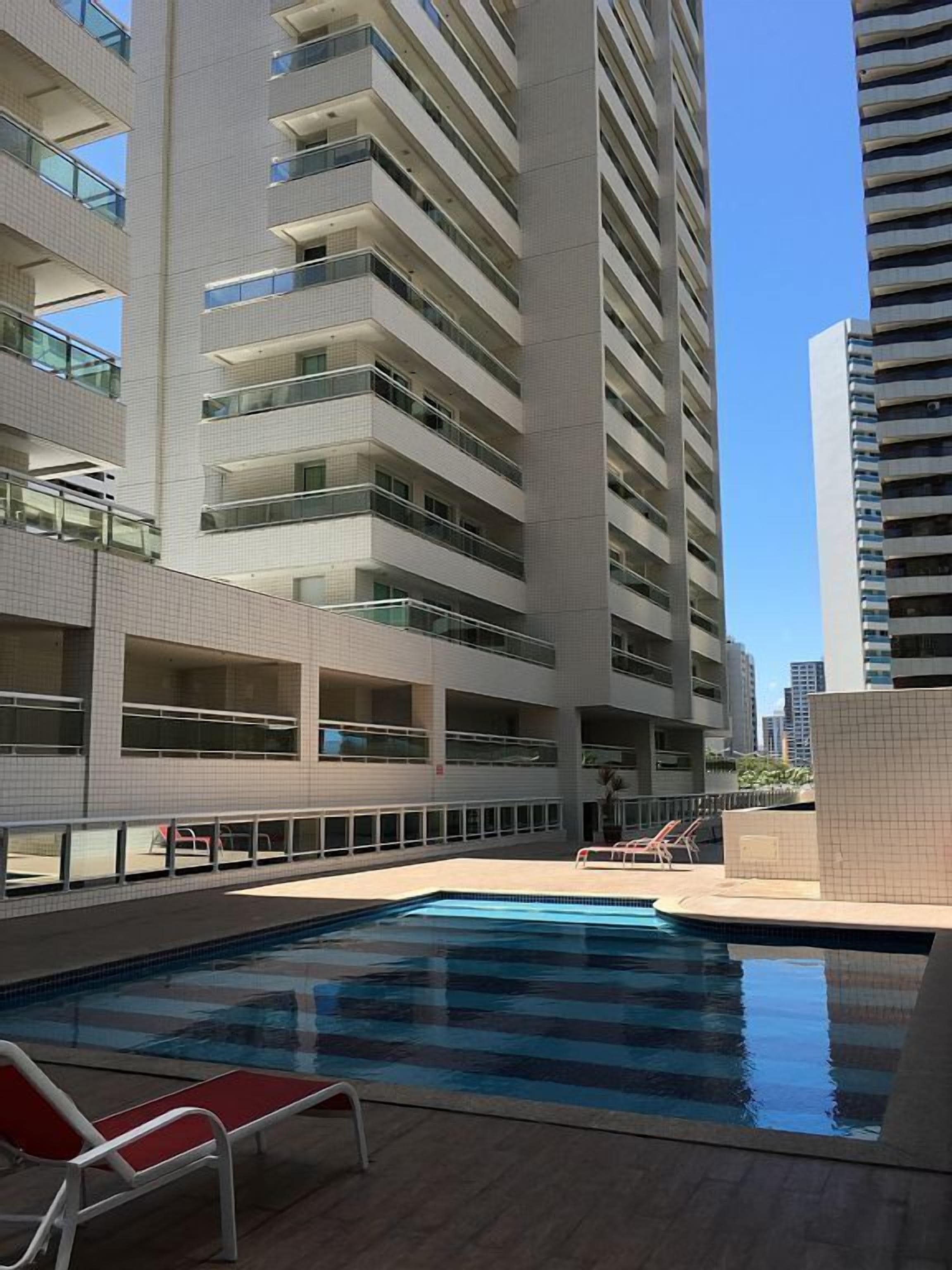 Un edificio moderno con área de piscina en la azotea, que cuenta con varios balcones y un cielo azul despejado.