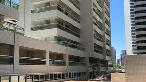 Un edificio moderno con área de piscina en la azotea, que cuenta con varios balcones y un cielo azul despejado.