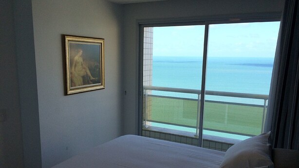 Un dormitorio con una cama grande, un cuadro en la pared y vistas al mar a través de un balcón.