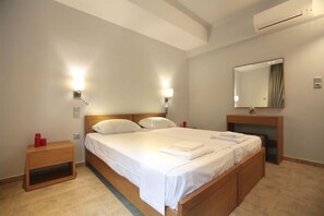 A hotel room with a large bed, bedside lamps, a nightstand, a mirror, and an air conditioning unit. - Meni Apartments Hotel (Athens)