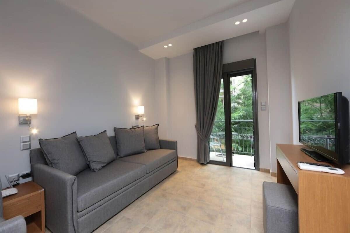 A modern living room with a grey sofa, a wooden side table, a TV, and a balcony with curtains.