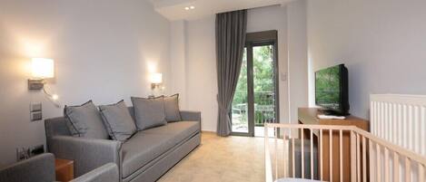 A modern living room with a grey sofa, a wooden crib, a TV on a wooden table, and a sliding glass door leading to a balcony.