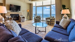 A spacious living room with a large TV, comfortable seating, a fireplace, and a balcony with a view of the ocean. - Turquoise Place 2806C (Orange Beach)