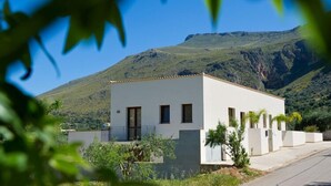 Un edificio moderno blanco con techo plano, rodeado de vegetación y un paisaje montañoso.