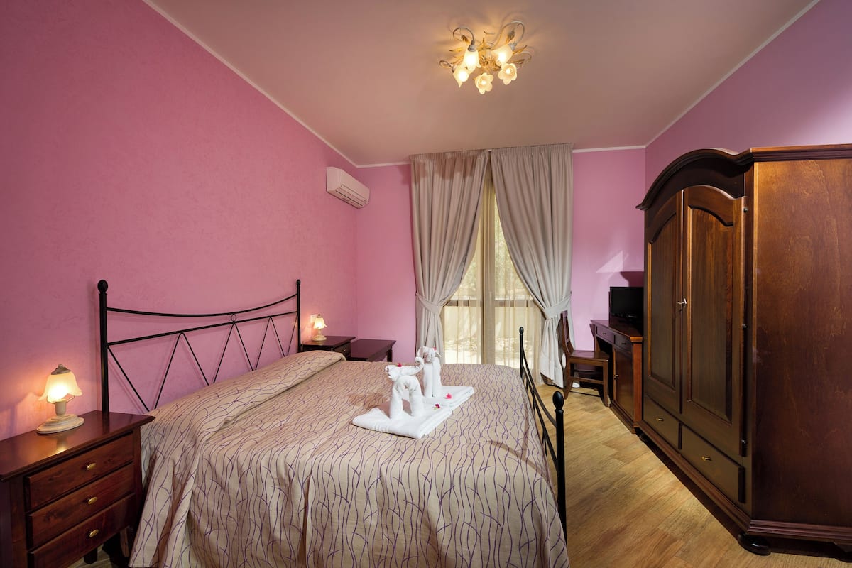 Une chambre à coucher avec un lit, une armoire, une télévision et une fenêtre avec des rideaux.