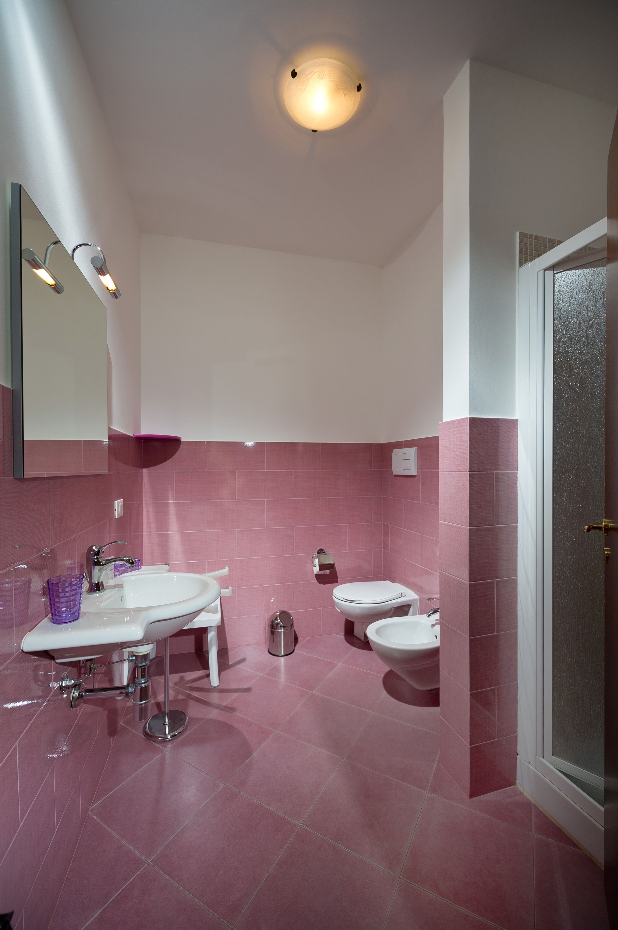 Un baño con azulejos rosas, un lavabo blanco, un espejo y una ducha.