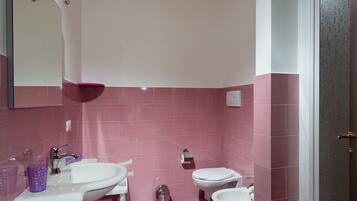 Un baño con azulejos rosas, un lavabo blanco, un espejo y una ducha.