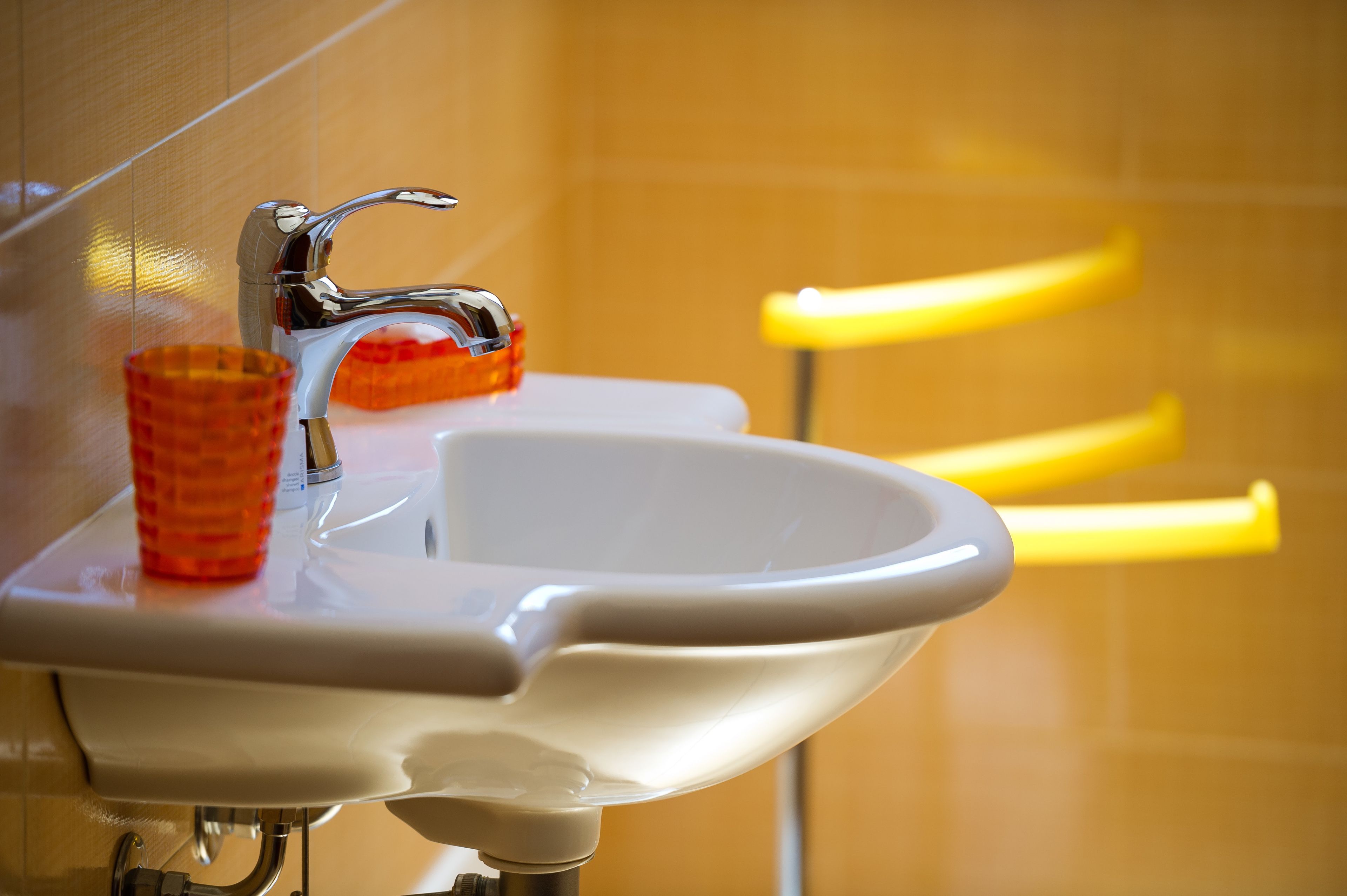 Un lavabo blanco con grifo cromado y una taza naranja.