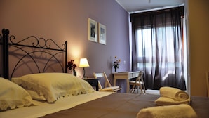 A neatly made bed with white linens, a desk with a chair, and a window with curtains. - Marcella House (Cagliari)