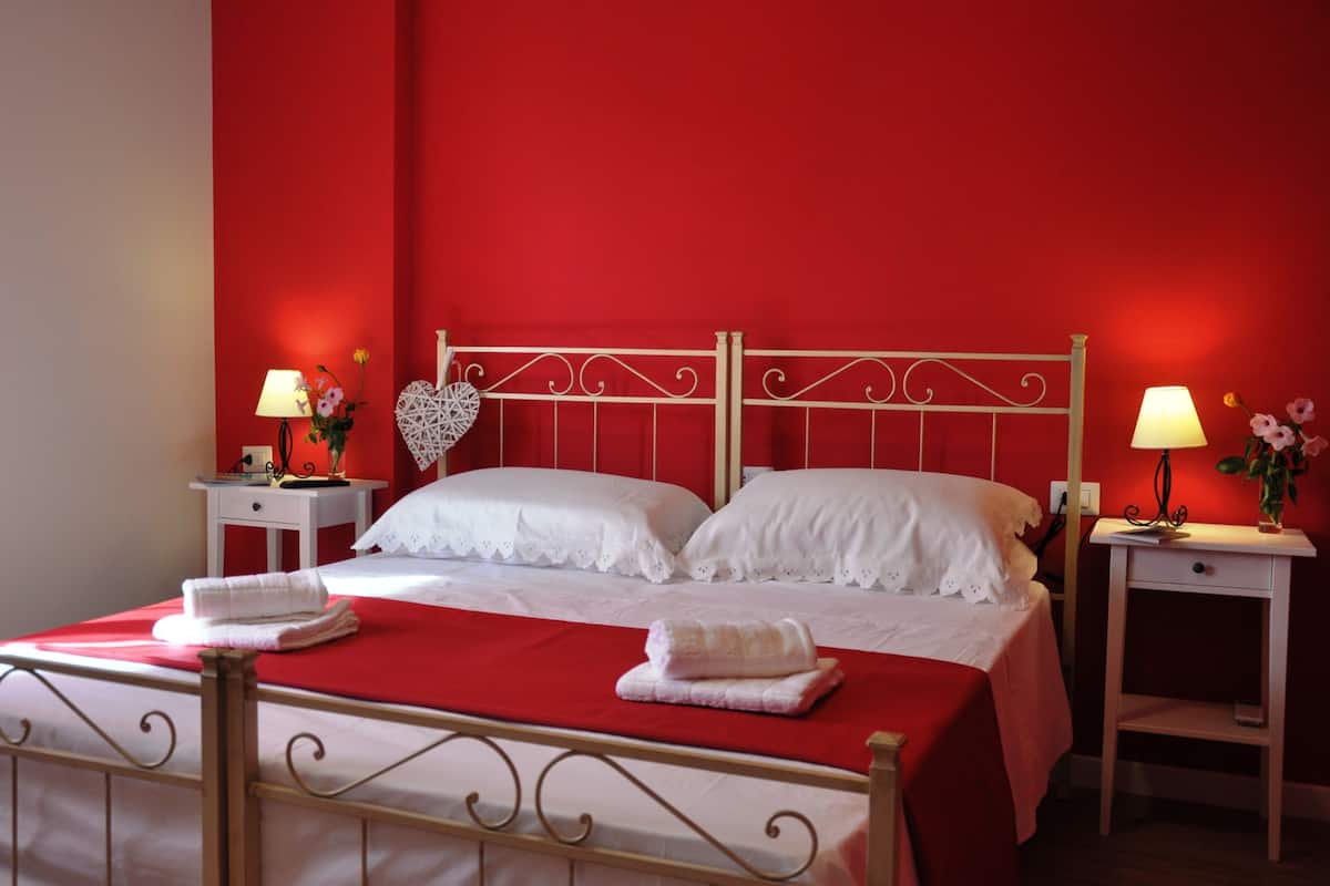Una cama bien hecha con sábanas blancas, dos mesitas de noche con lámparas y una pared roja.