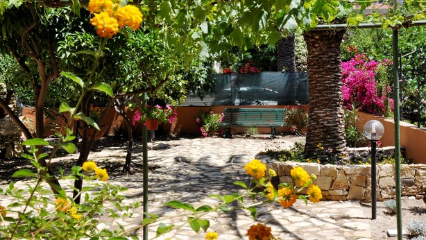 A garden with stone pathways, a pergola with yellow flowers, and a bench. - Marcella House (Cagliari)