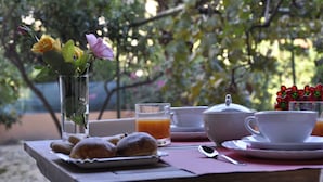 A table set with breakfast items including pastries, a glass of orange juice, a teapot, and a cup, with a vase of flowers in the background. - Marcella House (Cagliari)