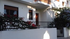 A white building with a balcony, a black metal railing, and red flowers in the foreground. - Marcella House (Cagliari)