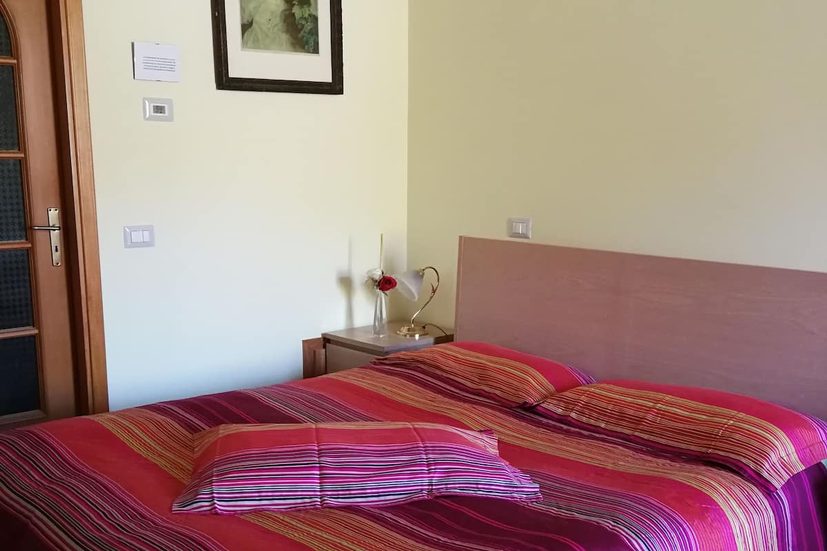 A room with a bed, a nightstand, a framed picture on the wall, and a door.