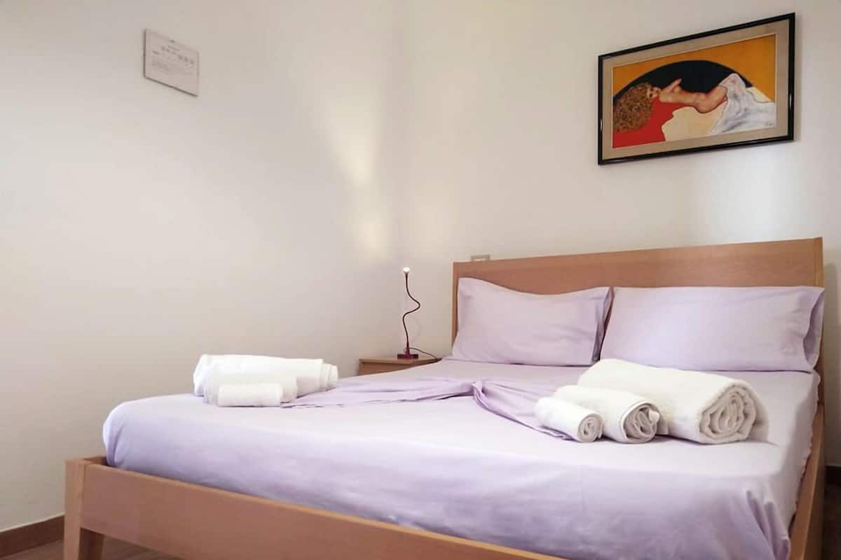 A neatly made bed with a wooden frame, a nightstand with a lamp, and a painting on the wall.