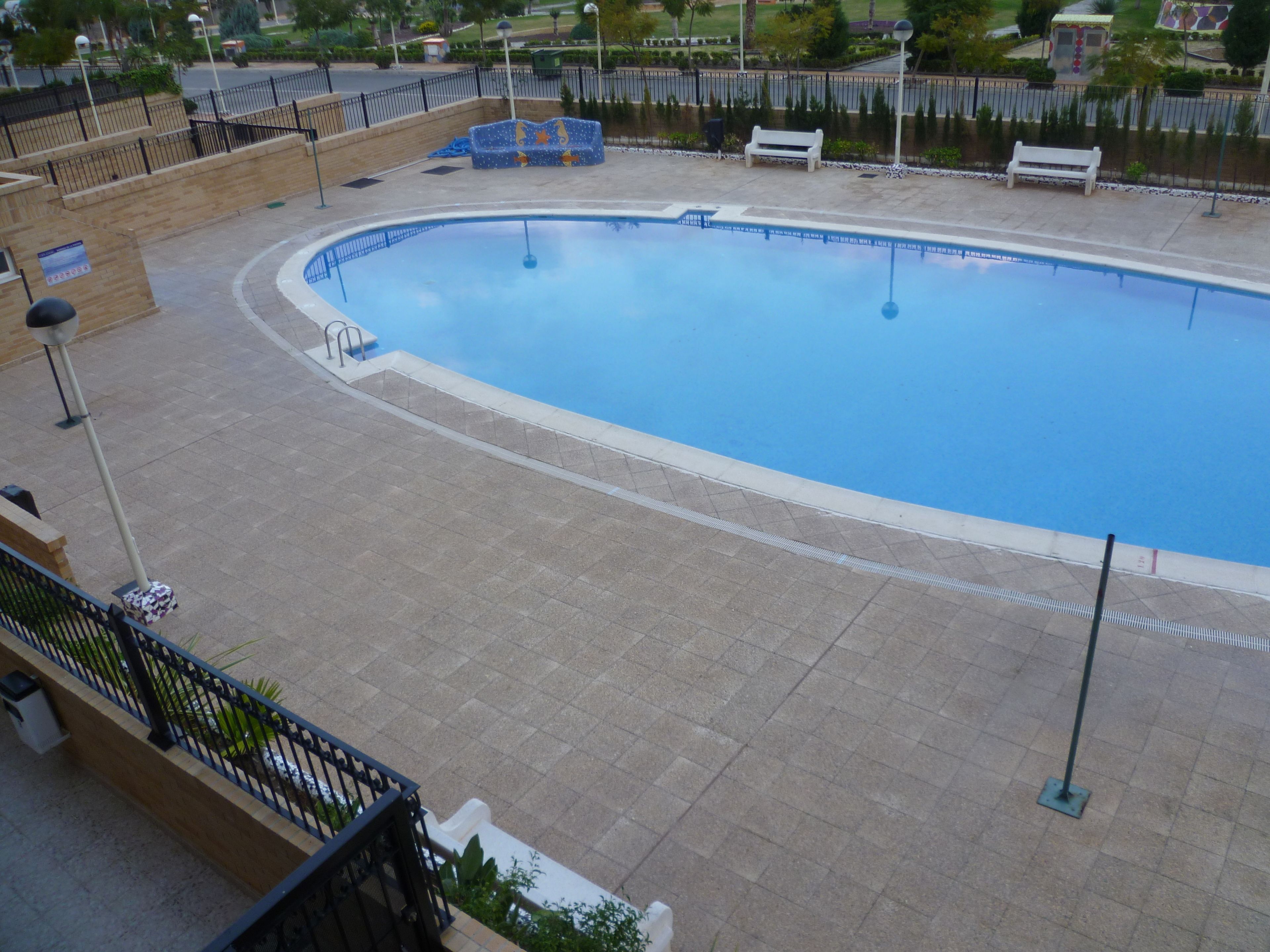 A swimming pool with a curved edge, surrounded by a tiled deck and benches.