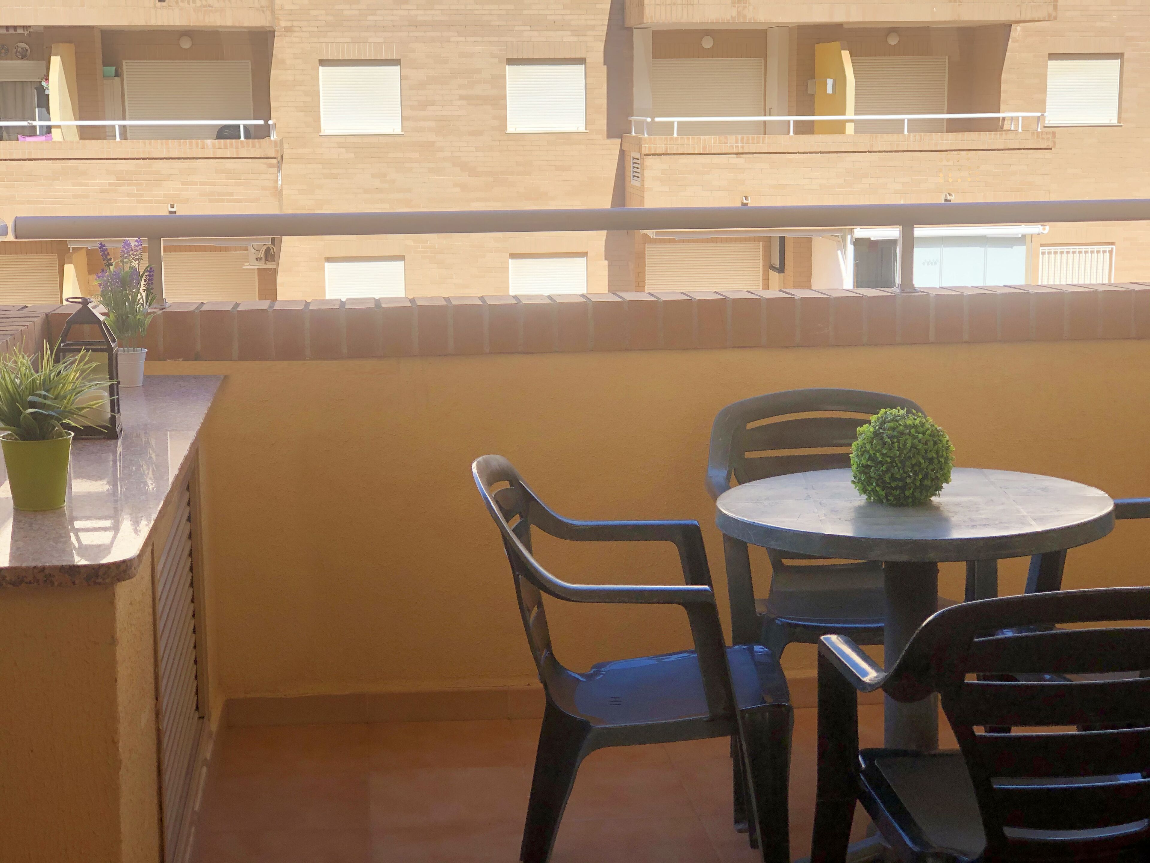 A balcony with a table and chairs, potted plants, and a view of a building with multiple windows.