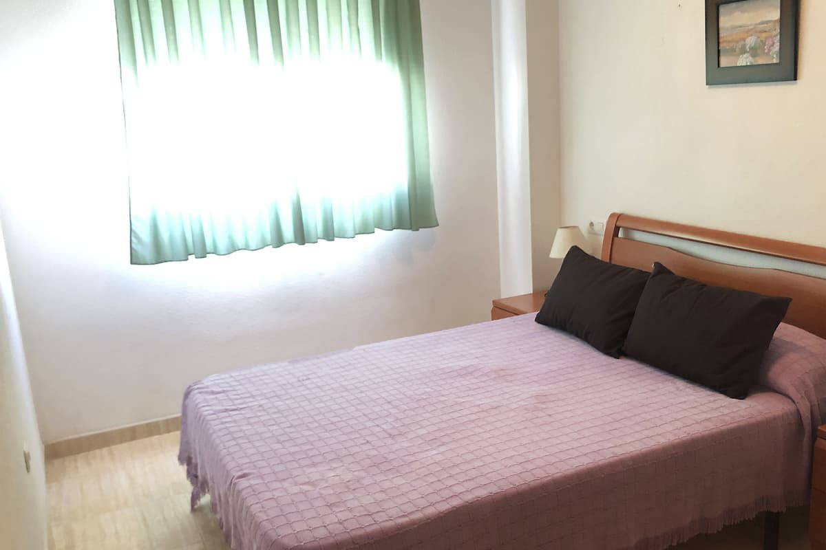 A bedroom with a bed, a nightstand, a lamp, and a window with curtains.