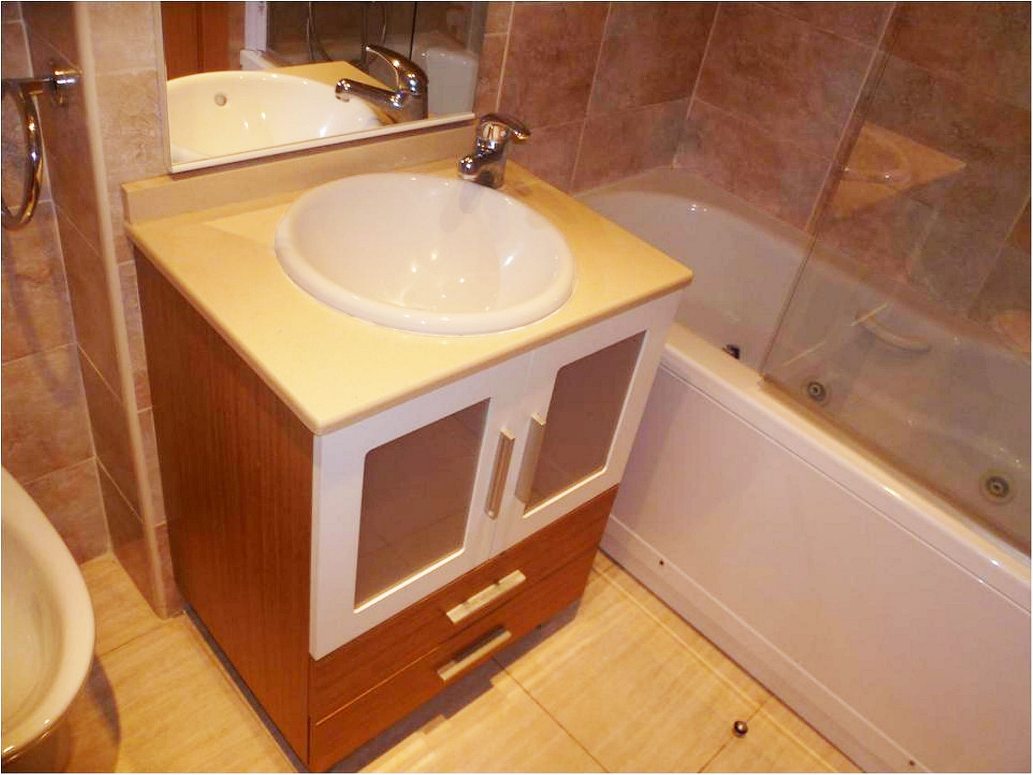A bathroom with a white sink, a mirror, a bathtub, and wooden cabinetry.