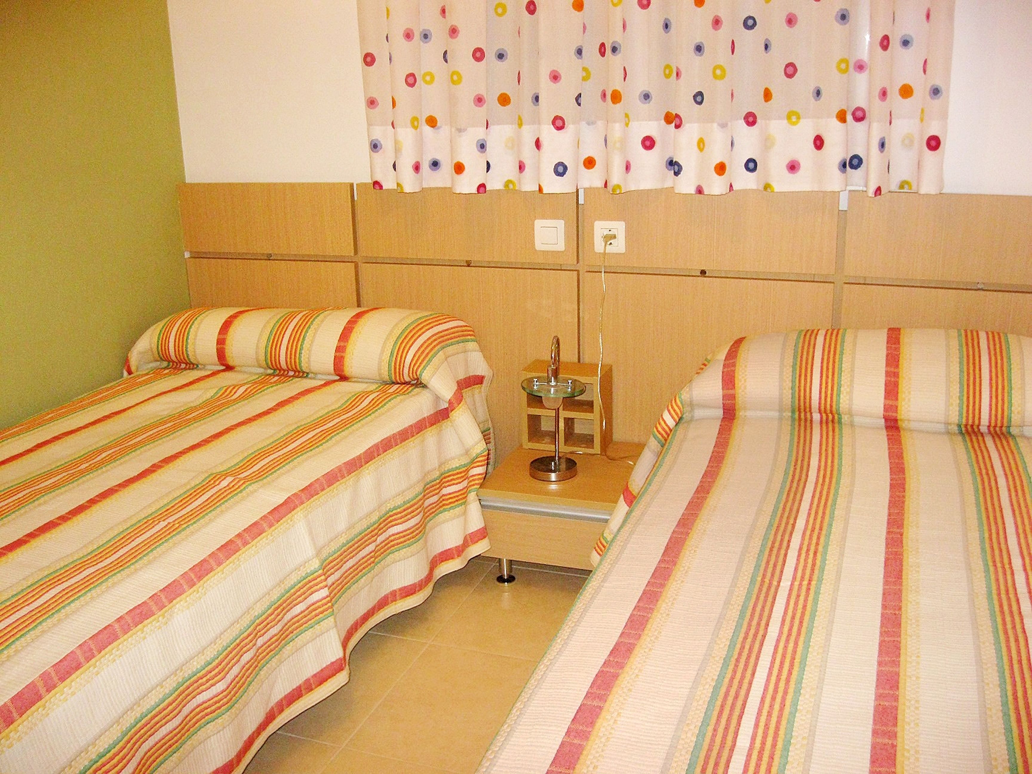 A hotel room with two beds, a small table with a lamp, and a curtain with a polka dot pattern.