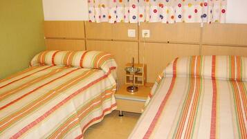 Habitación de hotel con dos camas, una mesita con una lámpara y una cortina de lunares.