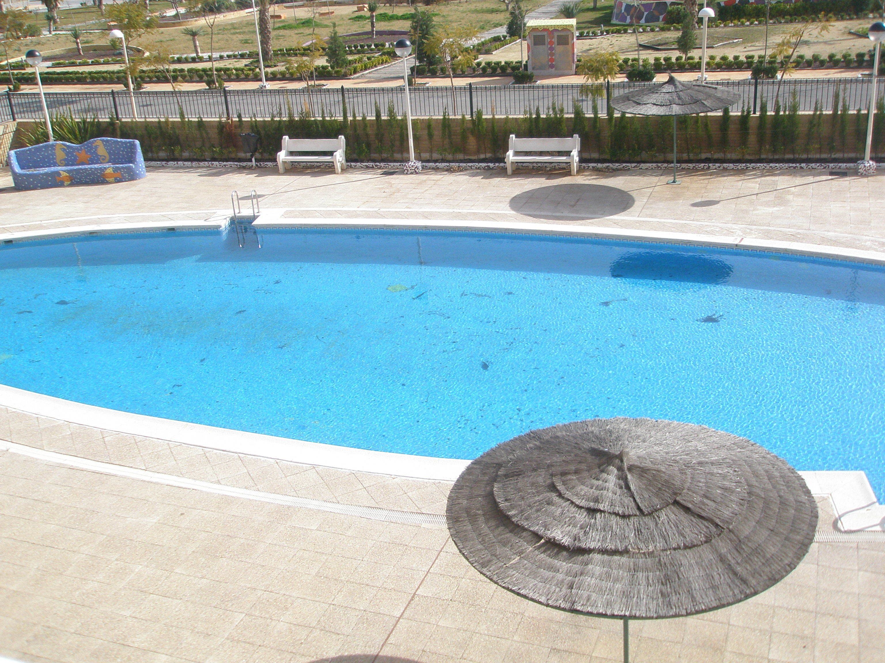 A swimming pool with a few lounge chairs and a sun umbrella.