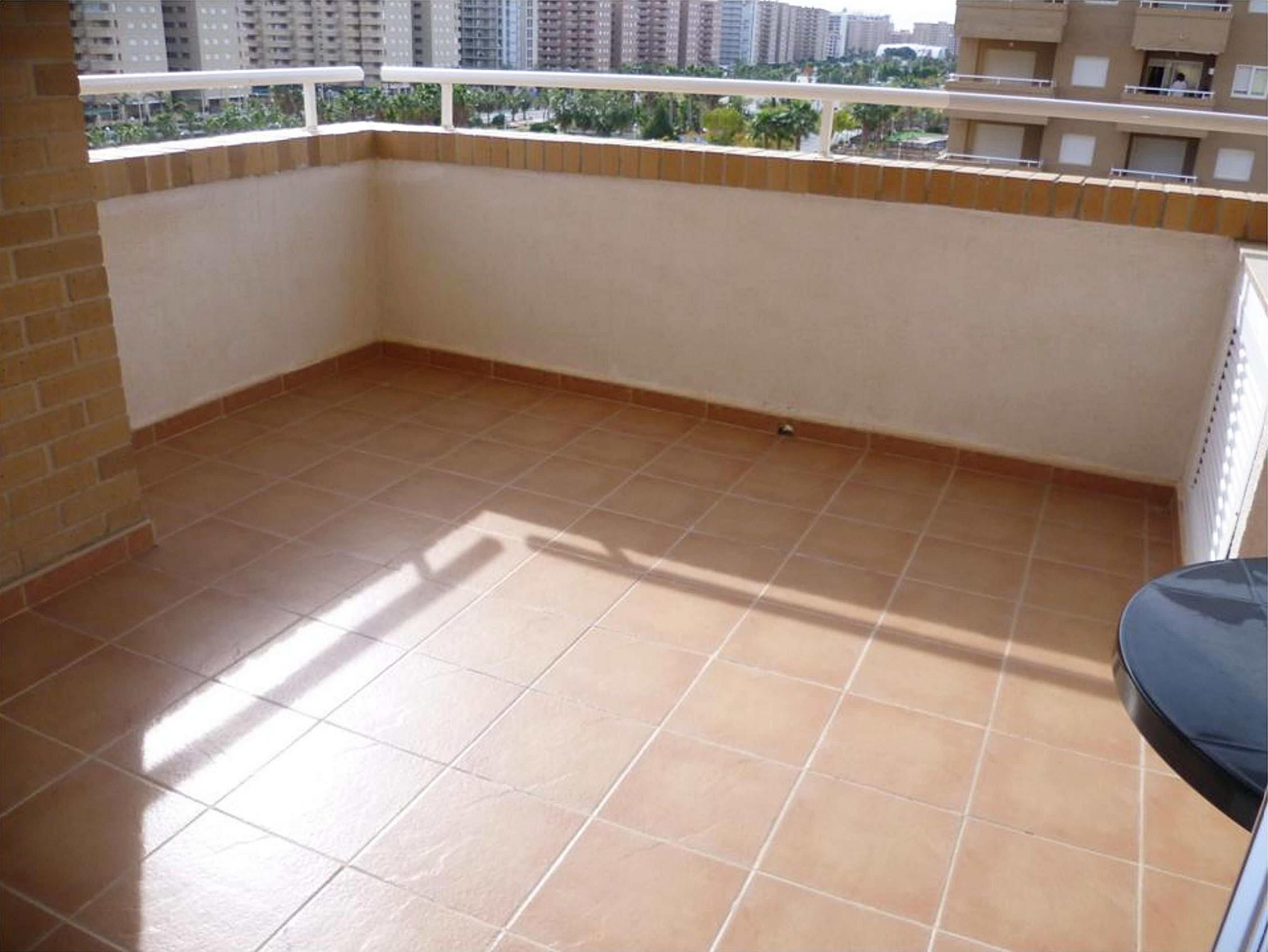A balcony with tiled flooring, a brick wall, and a view of surrounding buildings.