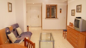 A living room with a sofa, a glass-top coffee table, a wooden cabinet, and a television. - Apartamentos Marina D'Or 3000 (Oropesa del Mar)