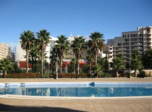 A swimming pool with a geometric tile pattern, surrounded by palm trees and a hotel building in the background. - Apartamentos Marina D'Or 3000 (Oropesa del Mar)
